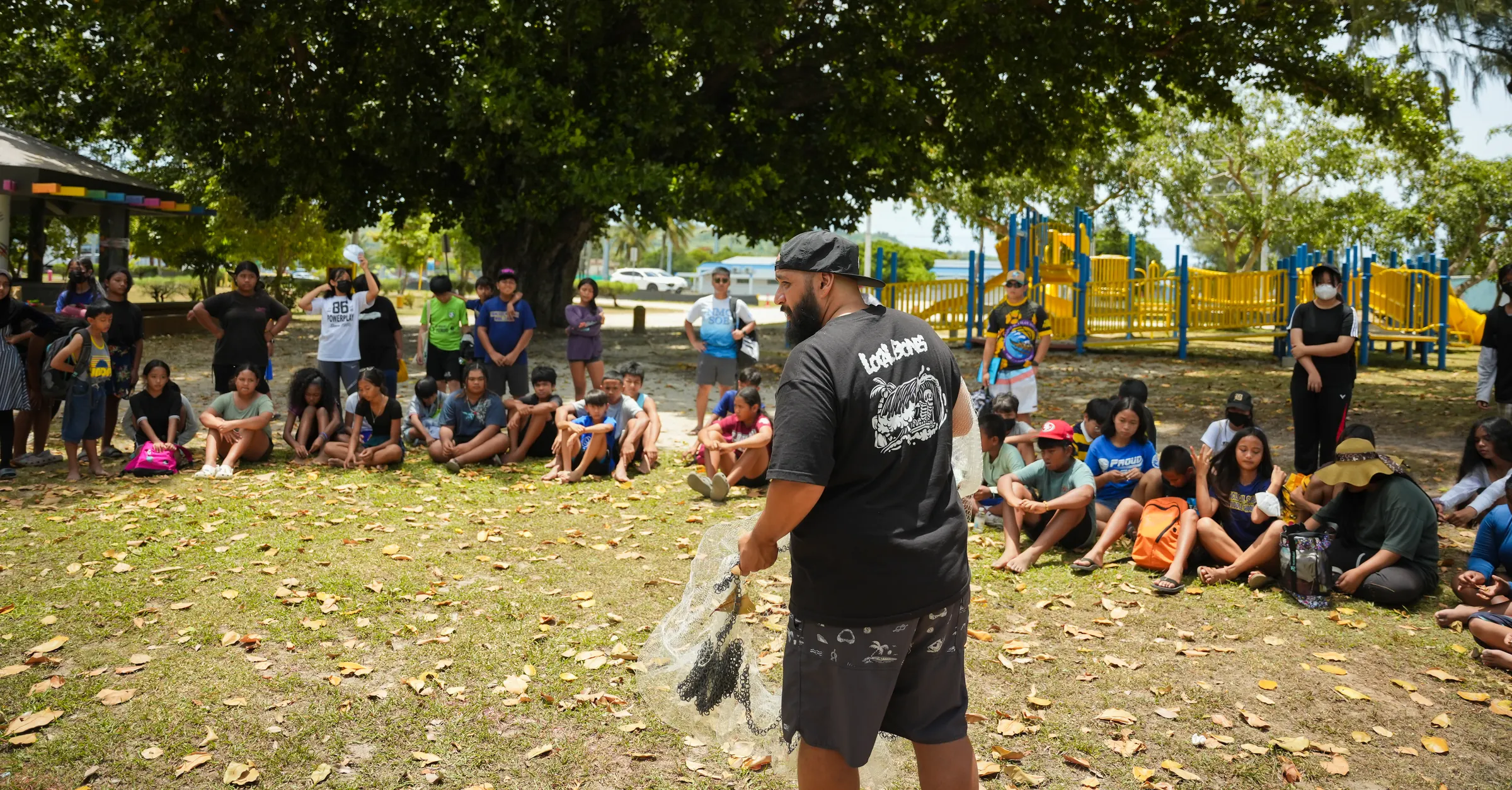 David Cabrera demonstrating a talåya net to a seated group under the trees