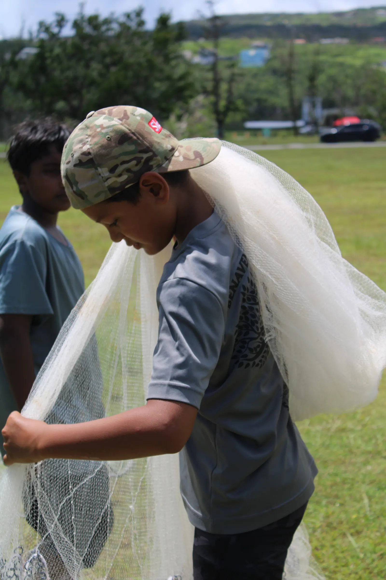 A young man in a camouflage cap gathering a talåya net over his shoulder