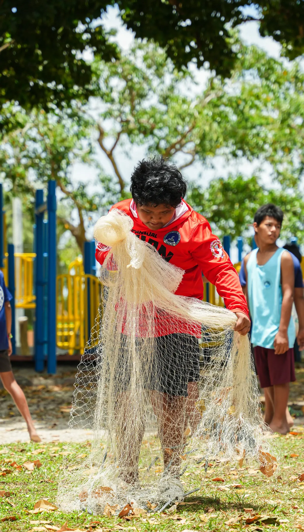 A young participant in a red shirt gathering a talåya net