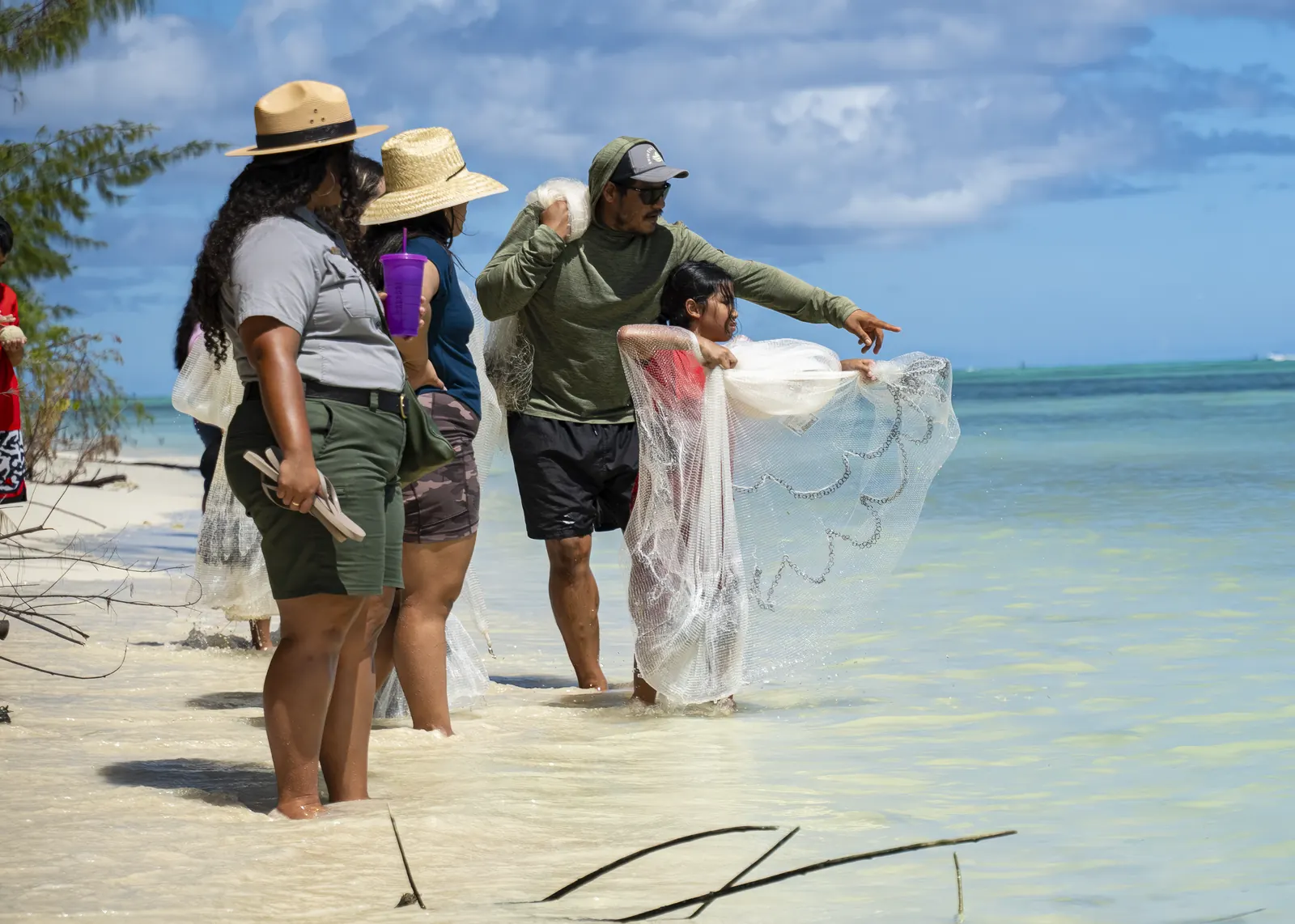 An instructor guiding two young people as they cast a talåya net in shallow water