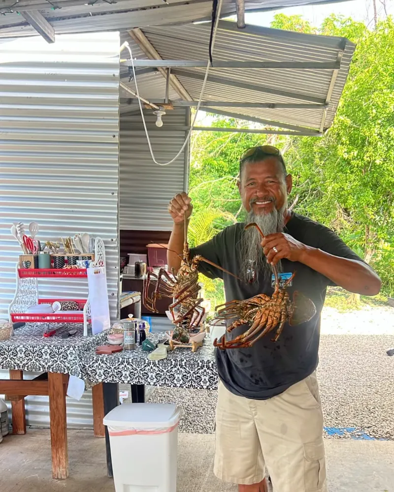 Cecilio Raiukiulipiy smiling and holding up two freshly caught lobsters