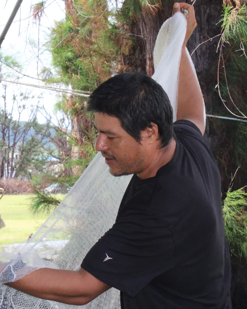 Jeremiah Benavente holding up a talåya net to untangle the line, beside a large tree